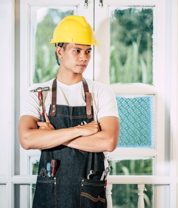 The carpenter stands and holds a hammer. Selective focus