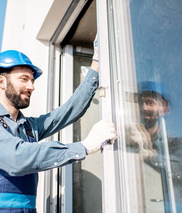 Workman in uniform mounting windows checking the level on the white building facade